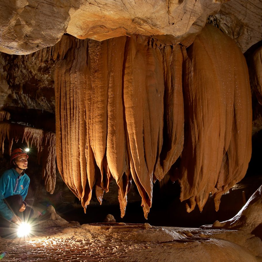 "Medusa" of calcite flowstone occupying a cave passage with caver next to it for scale