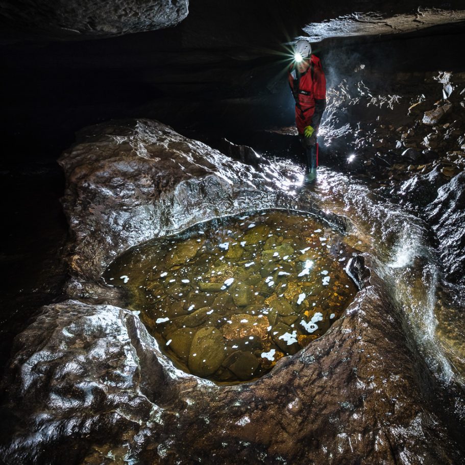 Caver lookinginto a cave gour with foam rafts and cobbles