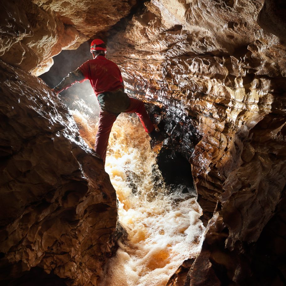 Caver climbing up a waterfall in a river passage