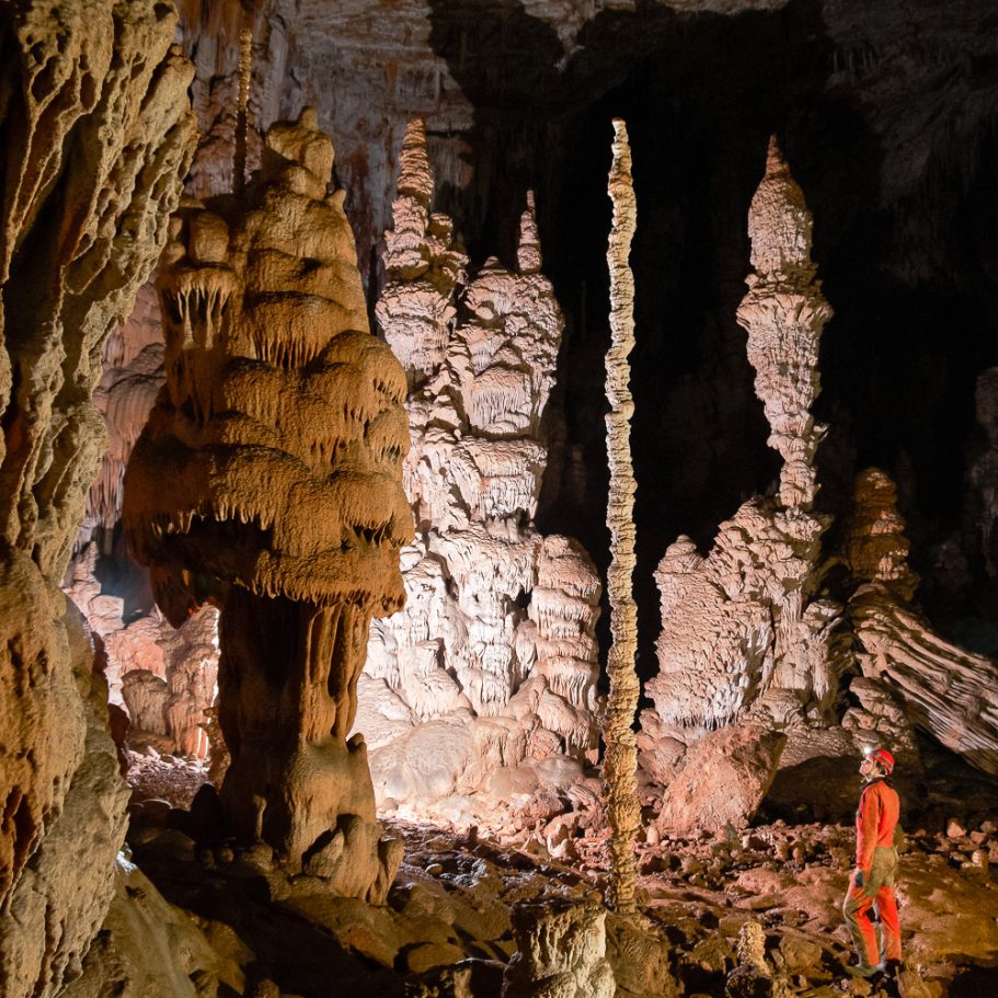 Caver in a large cave chamber with flowstone formations