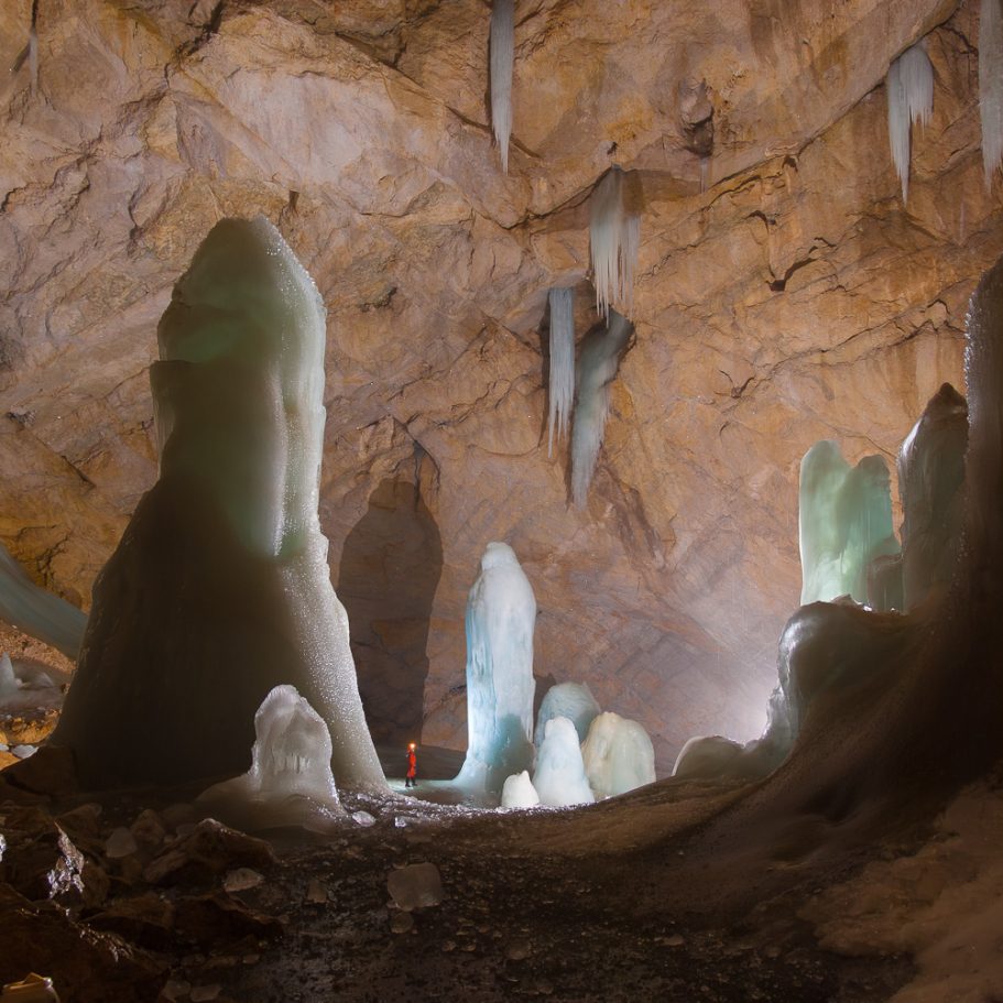 Giant cave chamber with a profusion of tall ice domes and cascades; a caver for scale appearing tiny in comparison