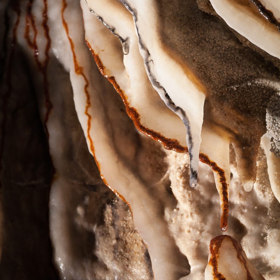 White calcite formations with brown and black streams of couloured flowstone on top
