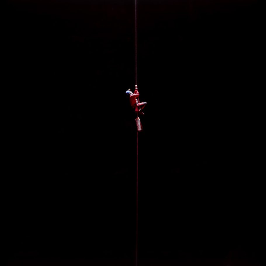 Caver climbing a rope with pitch black background