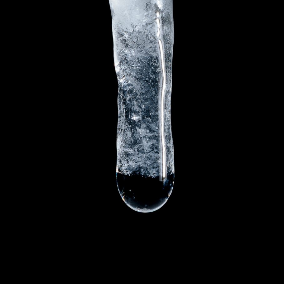 Macro-photo of an ice stalactite with a water drop forming at its tip