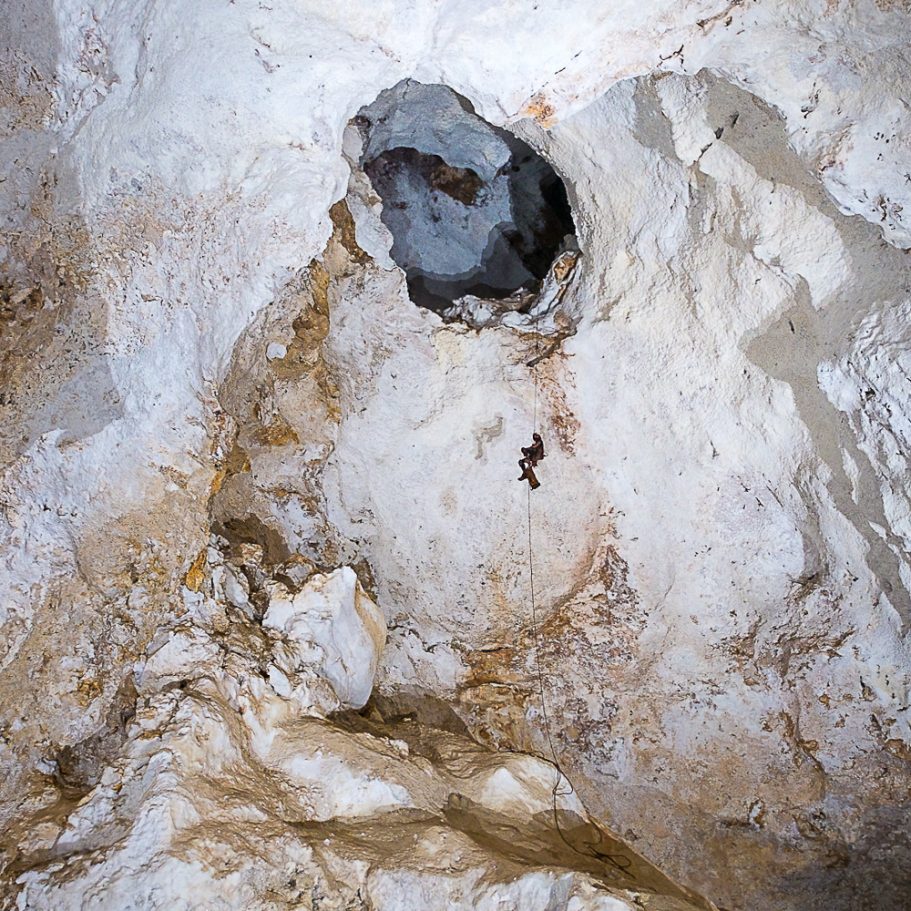 Caver climbing a rope in a tall cave dome