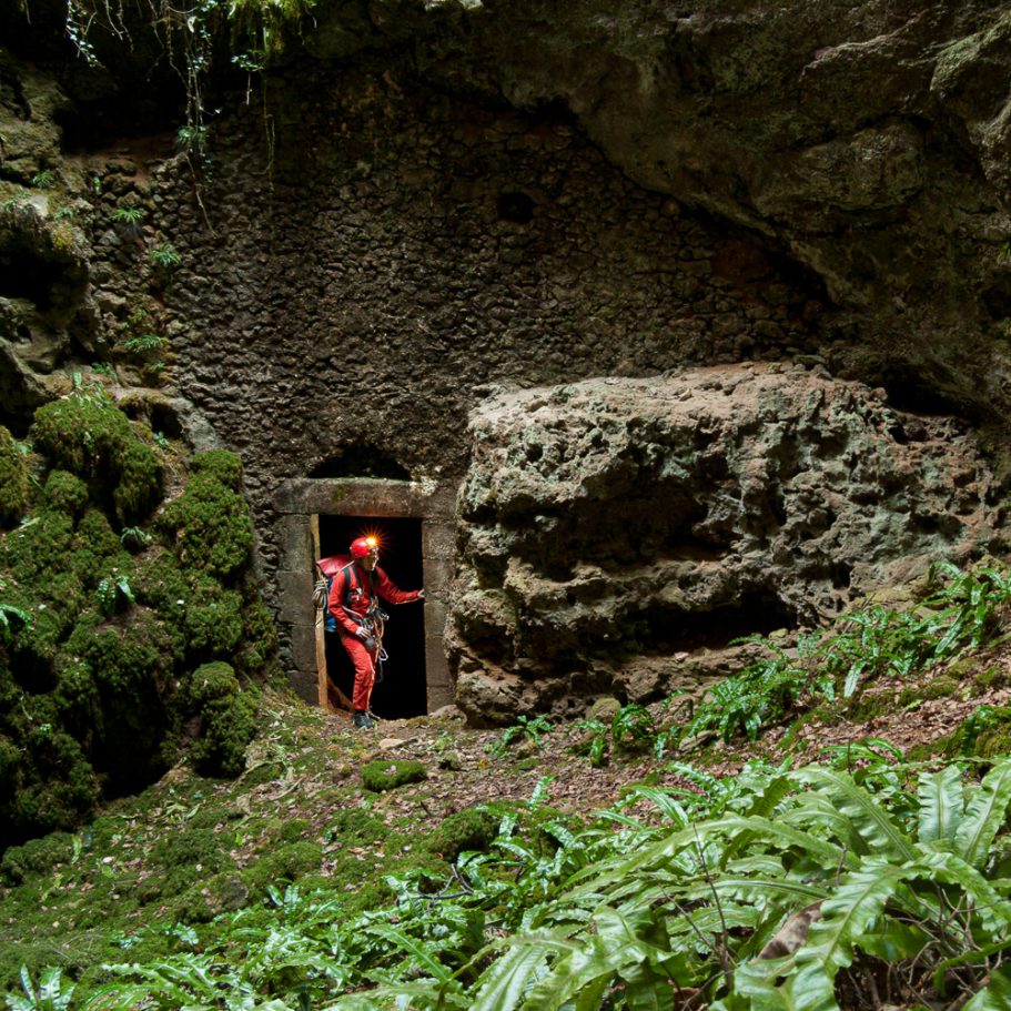 Stone wall with door in a cave passage with caver for scale