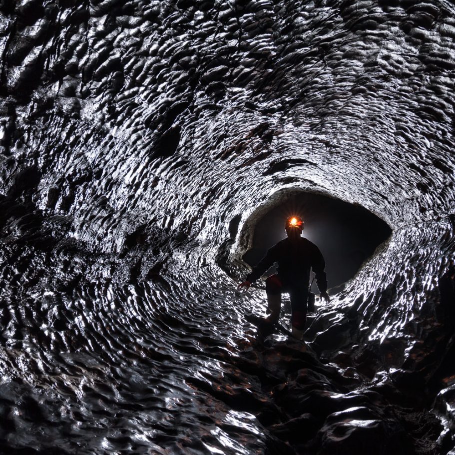 Caver in phreatic tube with reflecting scallops on the walls