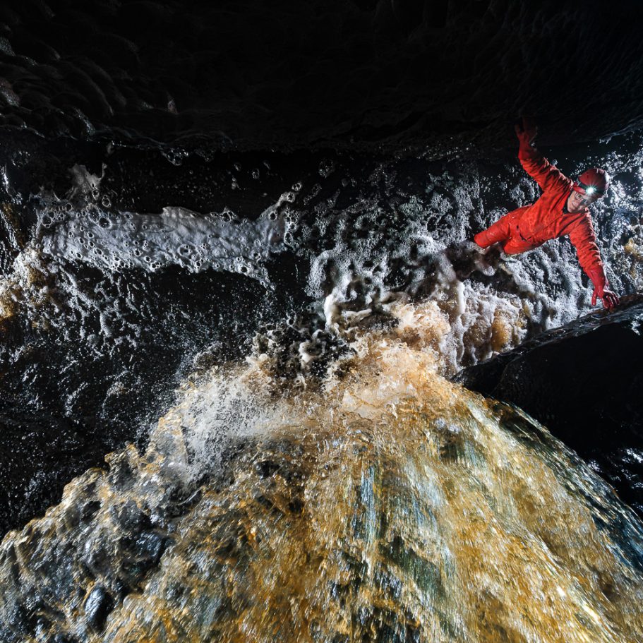 Underground waterfall seen from above with caver at bottom for scale
