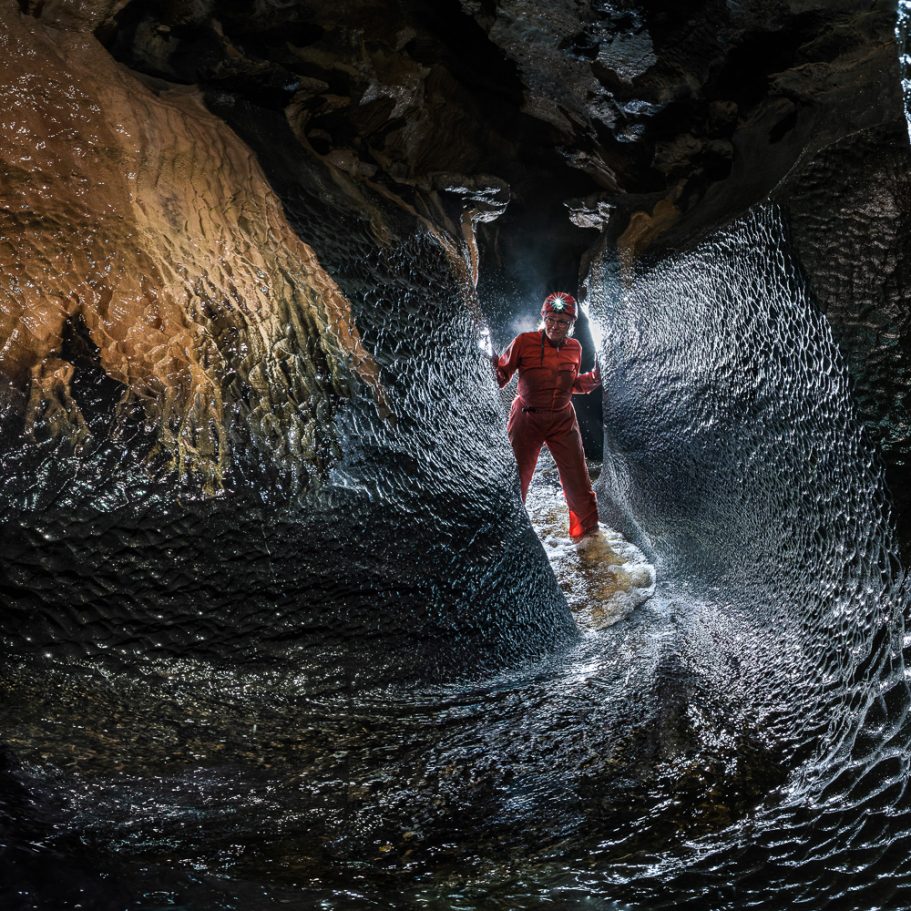 Caver in cave canyon with streamlet and scalloped walls