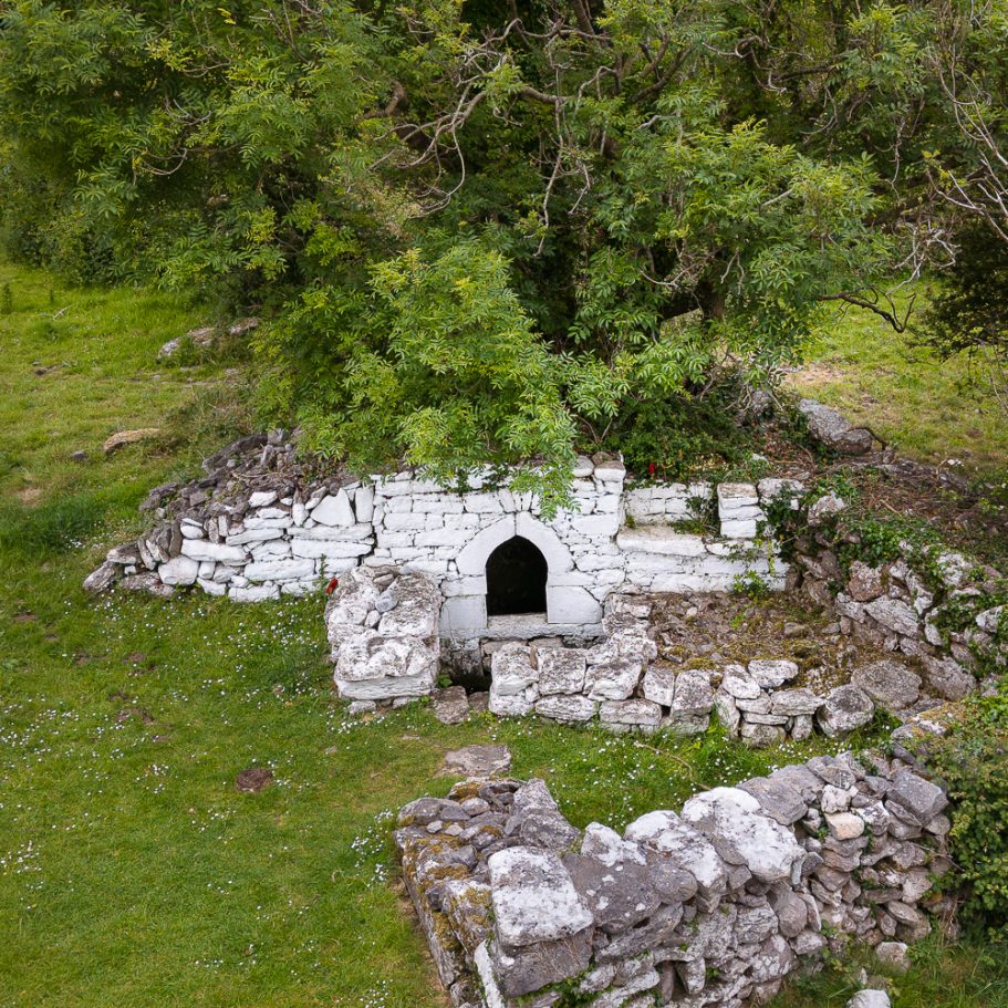 Holy well (karst spring) enclosed by white stone walls below a rag tree