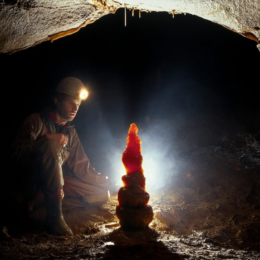 Caver looking at a stalagmite appearing deep-red in backlight