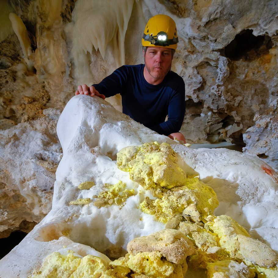 Cave explorer looking at junks of yellow elemental sulphur on a gypsum block in Lechuguilla Cave