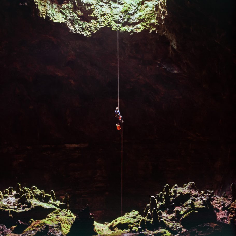 Caver rapelling from the entrance into a large cave passage