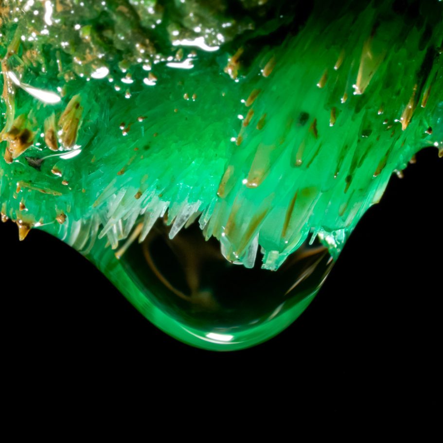 Close-up photo of a water droplet forming on green aragonite crystals