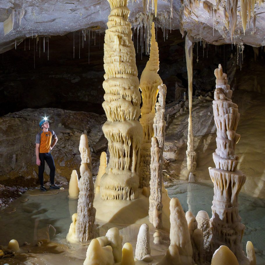 Caver for scale in a passage with pristine calcite stalagmites, stalactites, and columns in Lechuguilla Cave