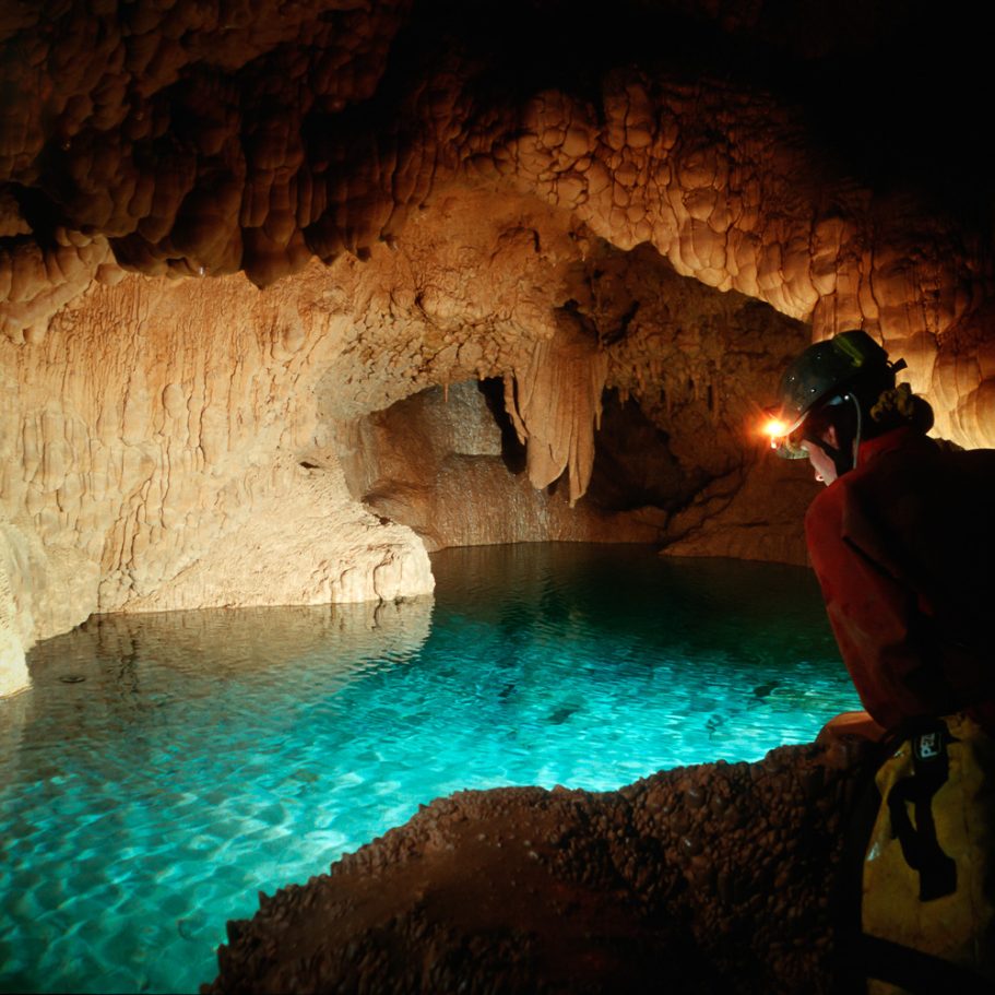 Caver looking into a blue cave pool