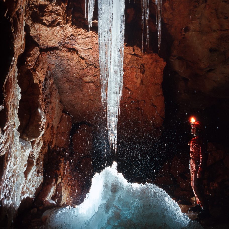 Caver next to ice stalactites dripping on a cave ice formation on the floor