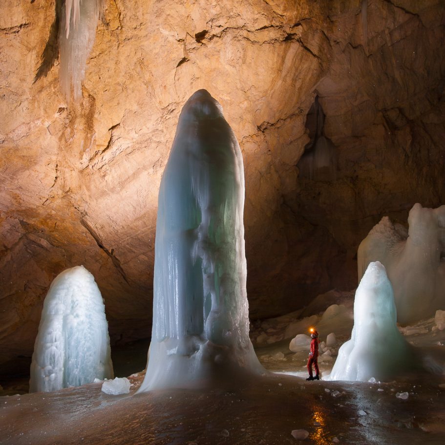 Three tall ice domes in a large cave chamber with a caver for scale