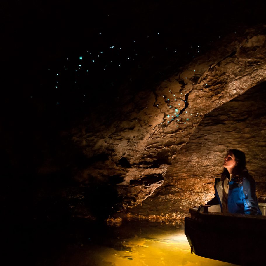 Caver in a boat on an underground lake with glowworms overhead
