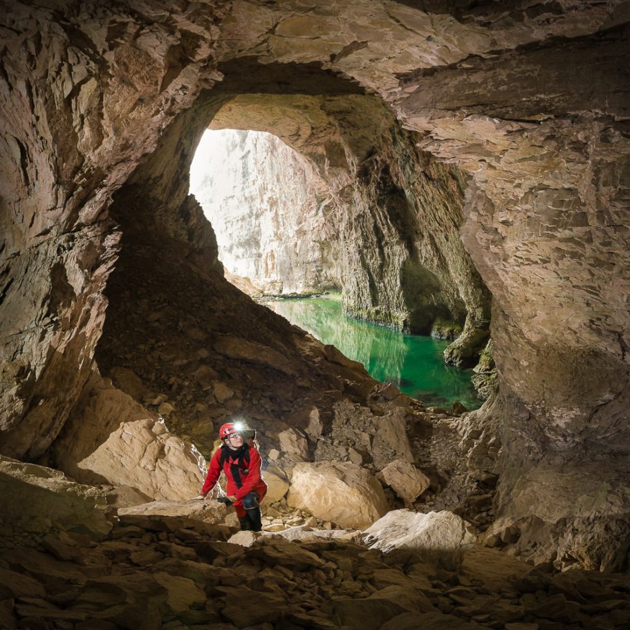 Caver scambling up blocks in cave entrance with a lake