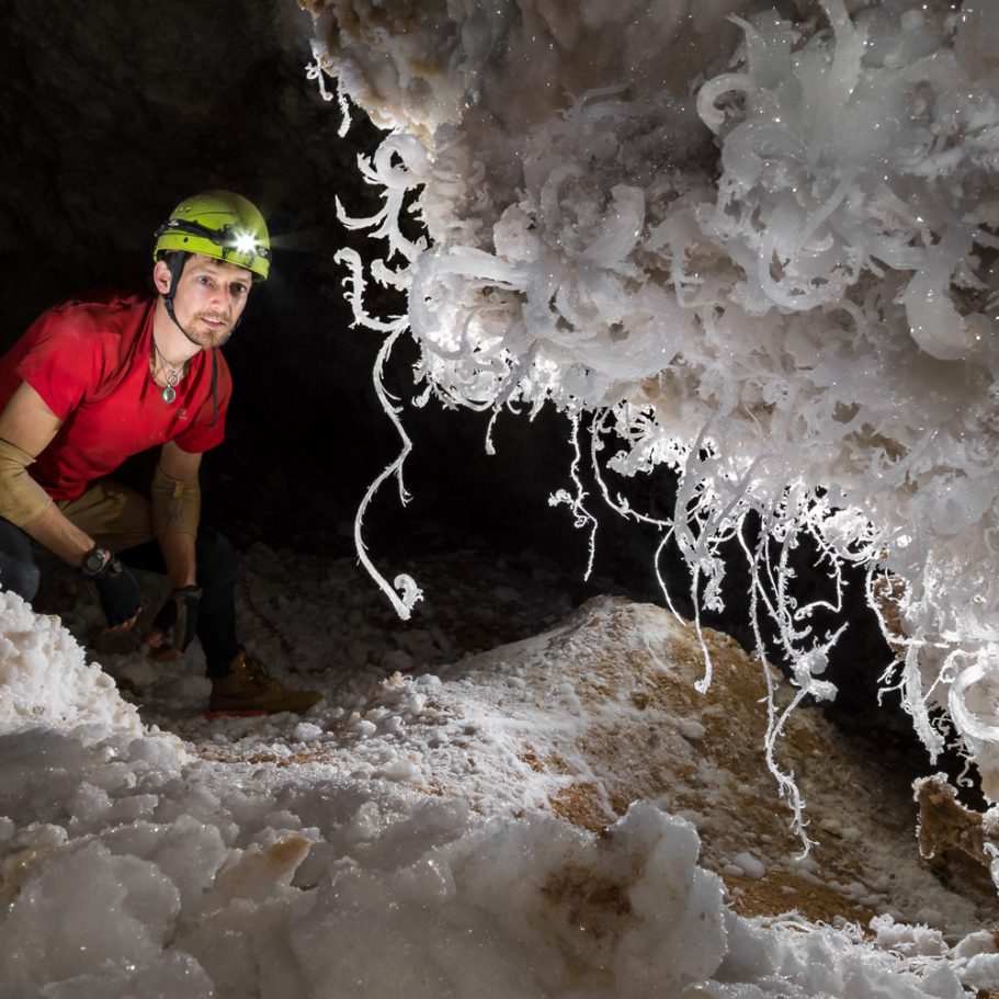 Caver looking at twisted and curled gypsum "flowers" on the cave wall