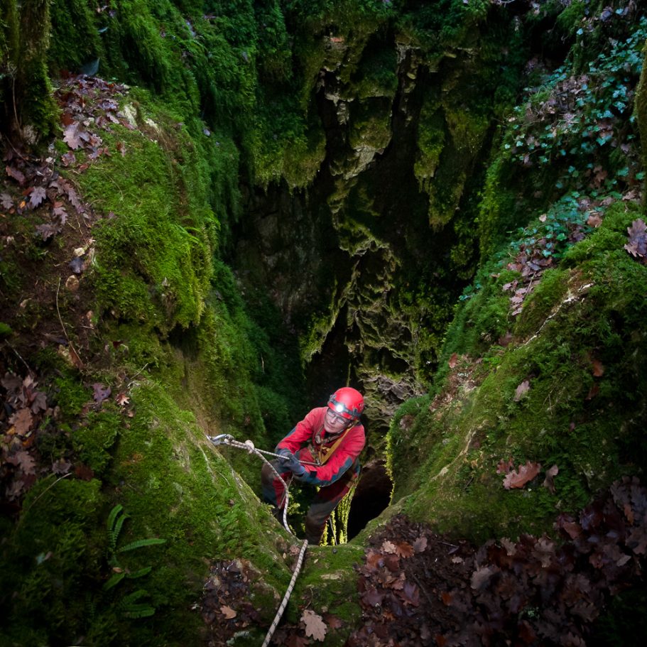 Caver climbing a rope back out of a pit covered in moss