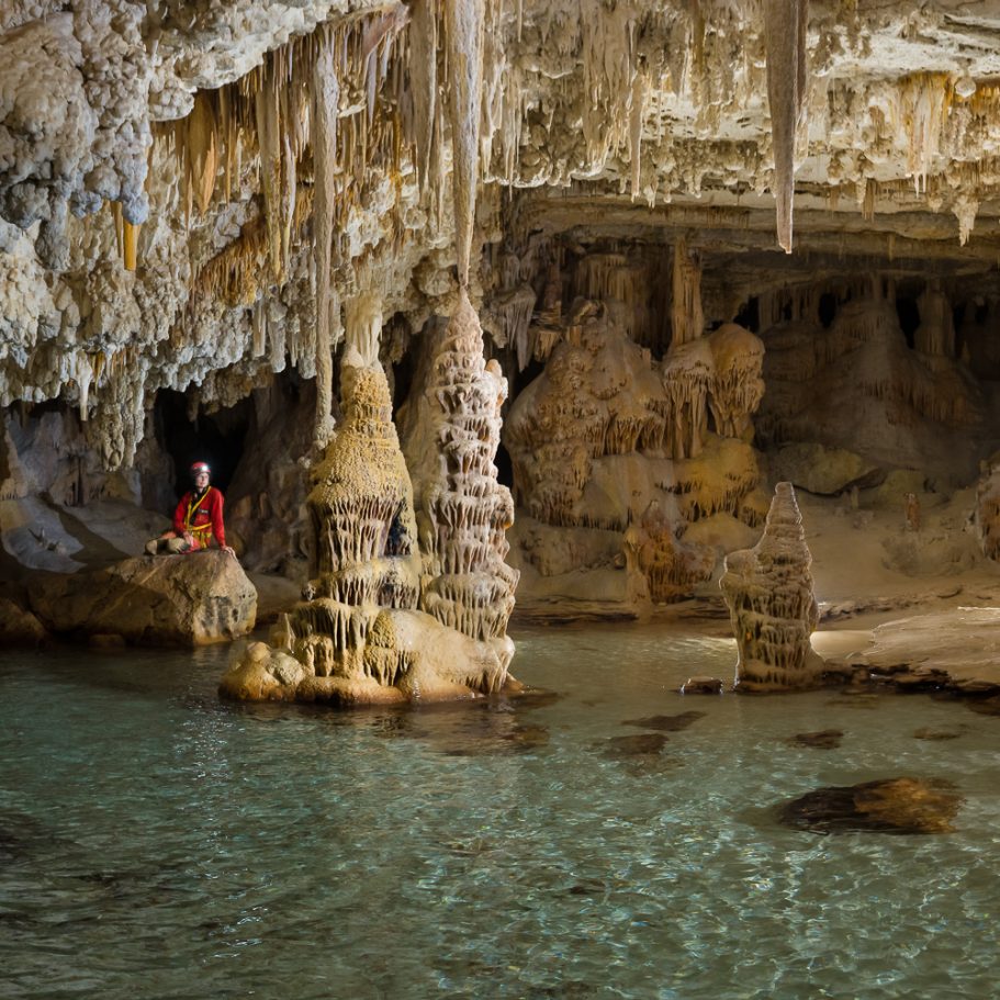 Underground lake surrounded by flowstone formations and a caver for scale