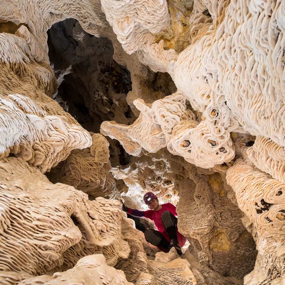 Looking upwards in a cave passage covered in cave folia speleothems in Lechuguilla Cave; caver for scale