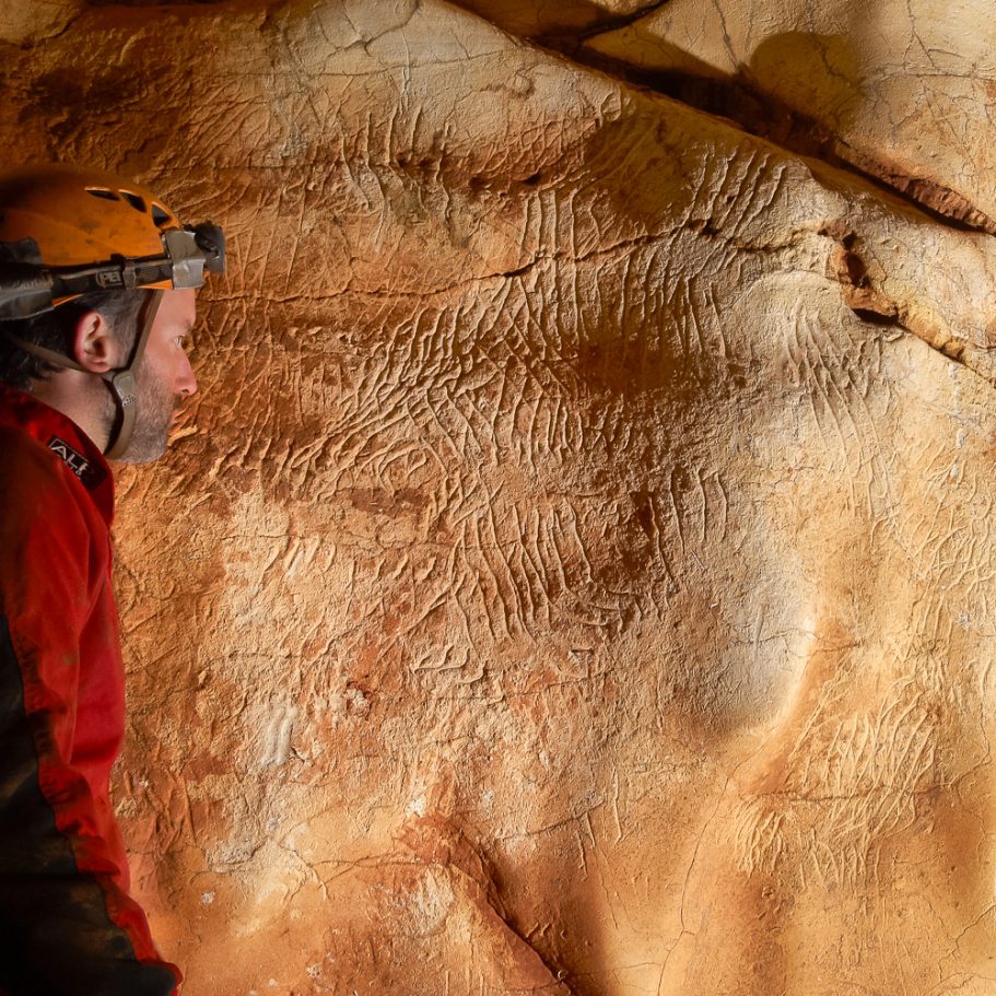 Cave explorer inspecting a cluster of claw marks on the wall of a cave