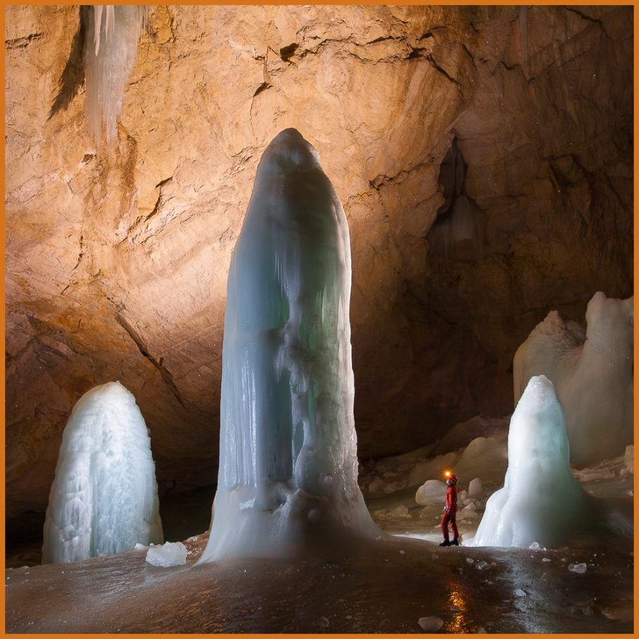 Three tall ice domes in an ice cave with a caver appearing small besides them; title photo for "Alpine Ice Caves" portfolio