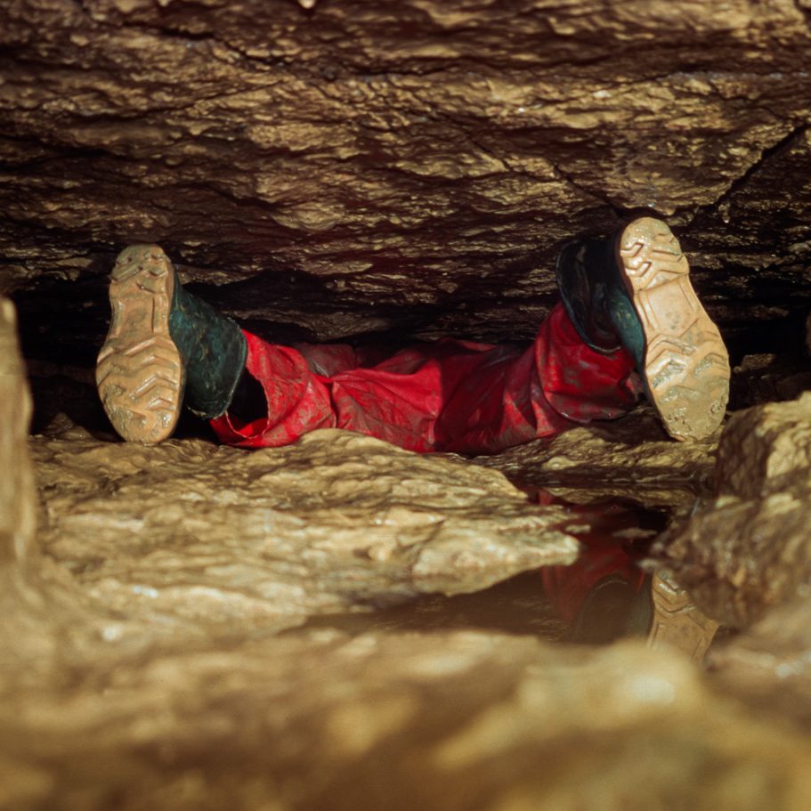 Boots of a caver squeezing through a very low passage