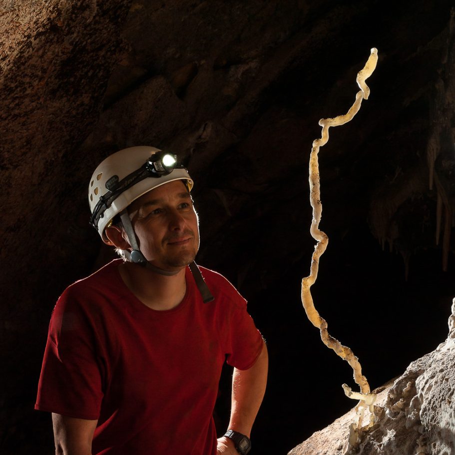 Caver admiring a tall snake-dancer helicite growing upwards from the flowstone
