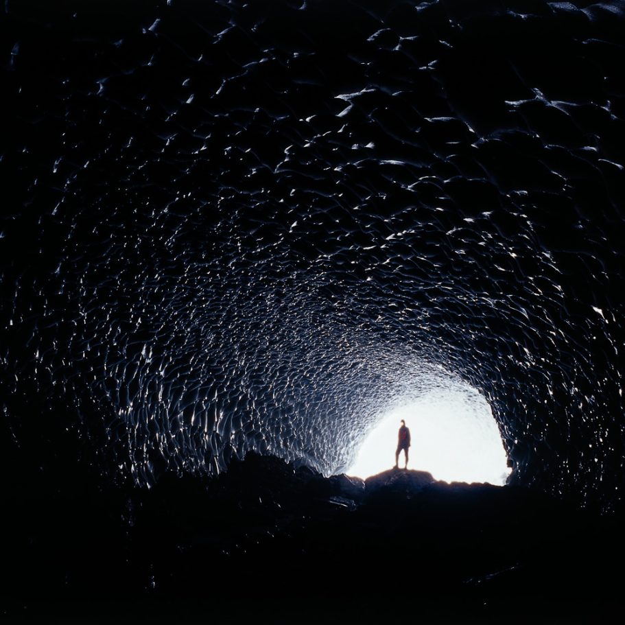 Caver entering a glacier cave with scalloped ice walls