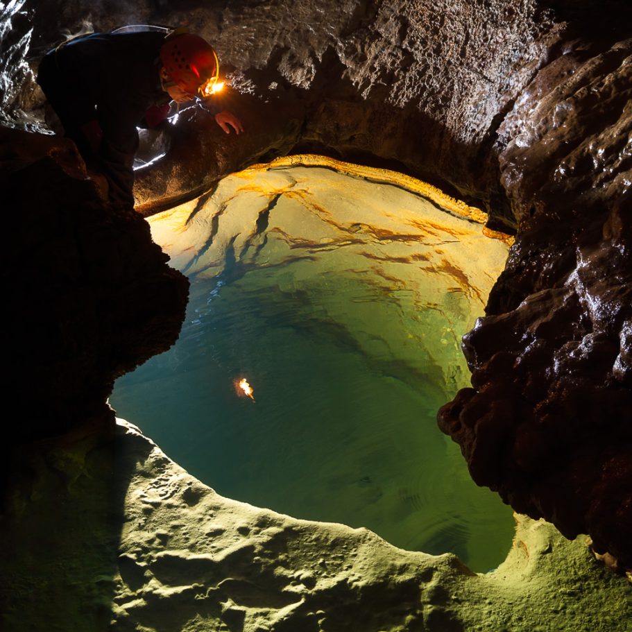 Caver looking into a cave gour, the walls of which appearing golden