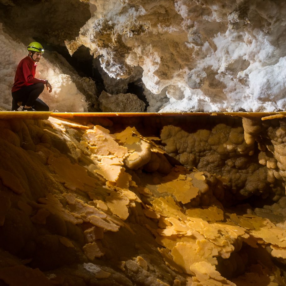 Caver on the rim of a dry lake in Lechuguilla Cave with large calcite rafts covering the bottom