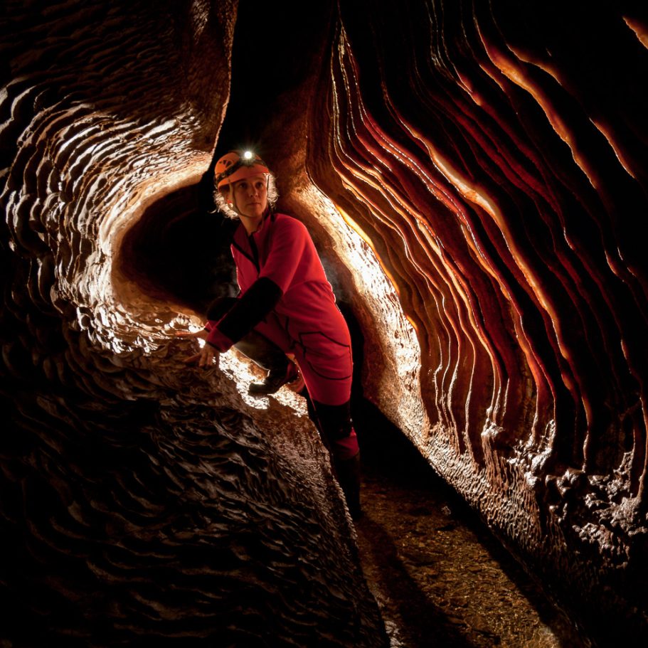 Cave passage with streamlet and calcite draperies on the walls; caver in the centre