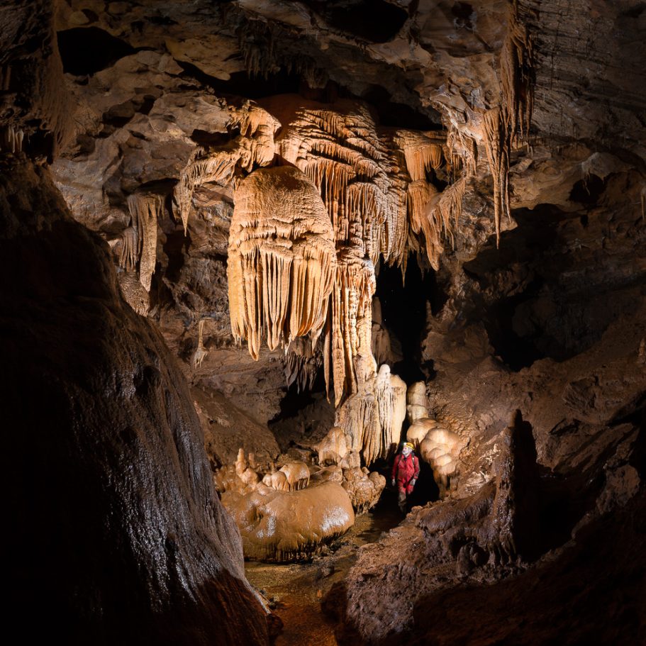 Caver in a river cave with flowstone formations
