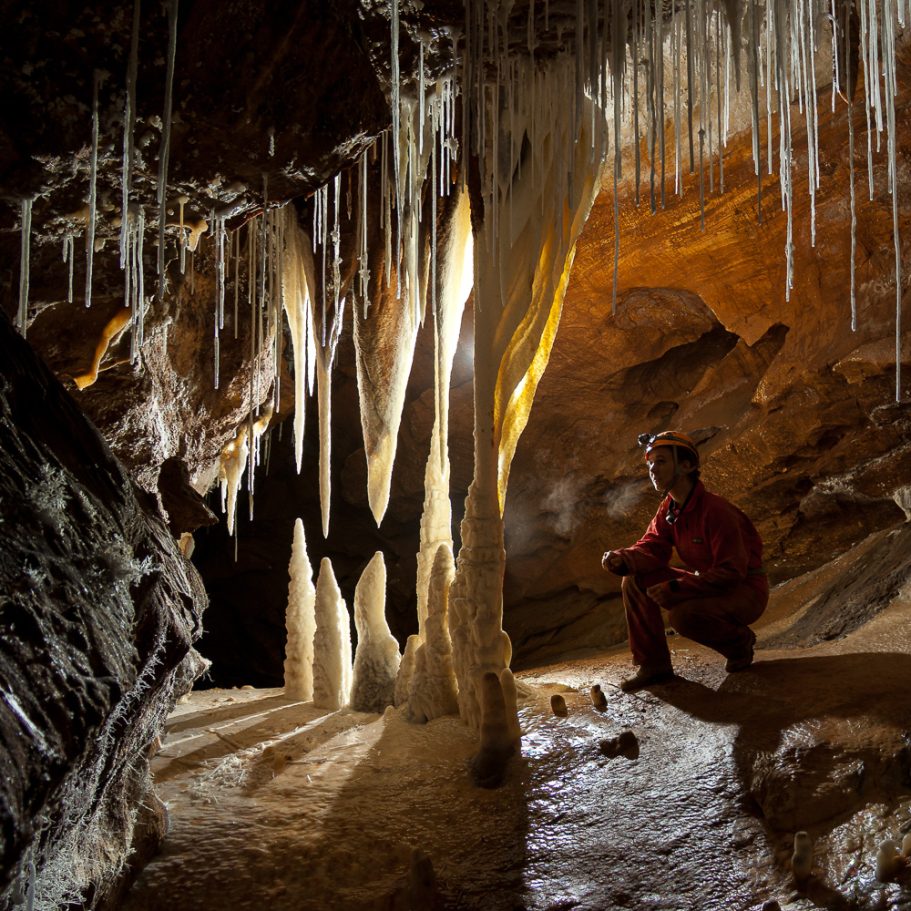 Group of white cave mineral formations with a cave explorer next to it