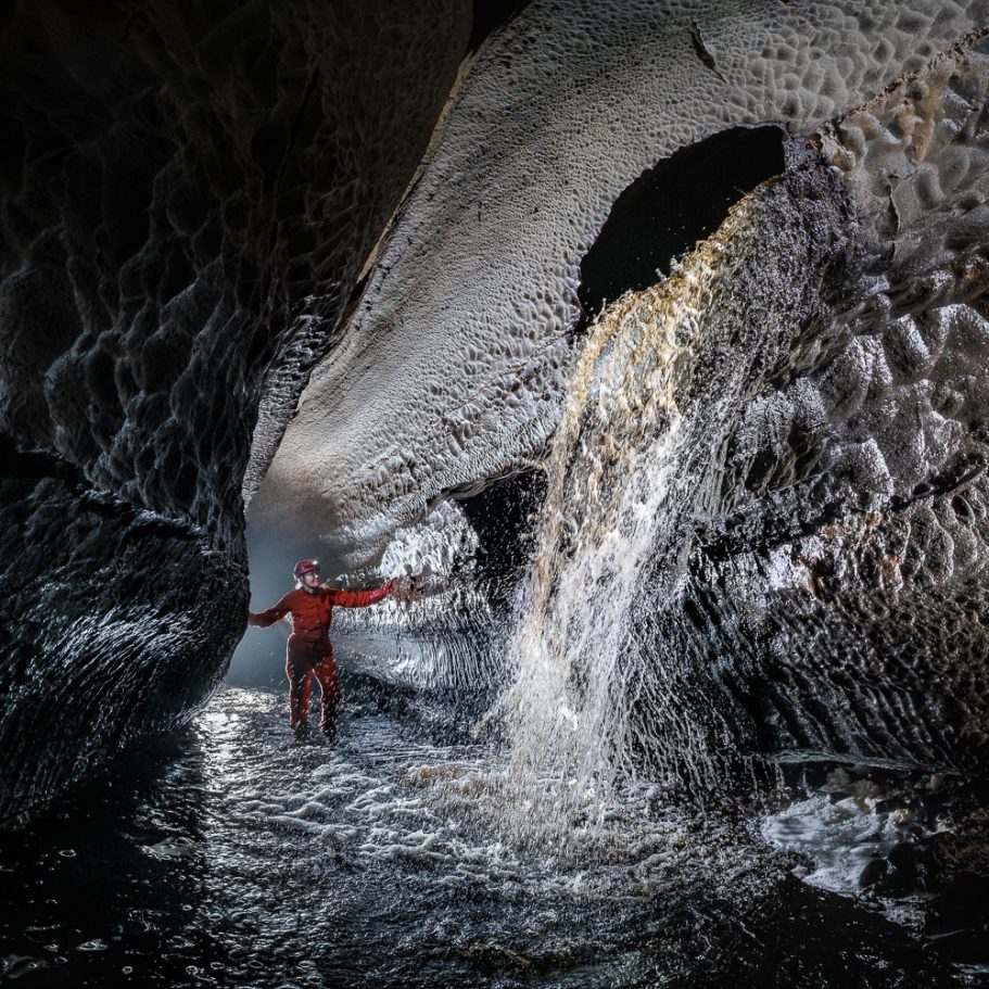 Caver in cave stream looking at roaring underground waterfall