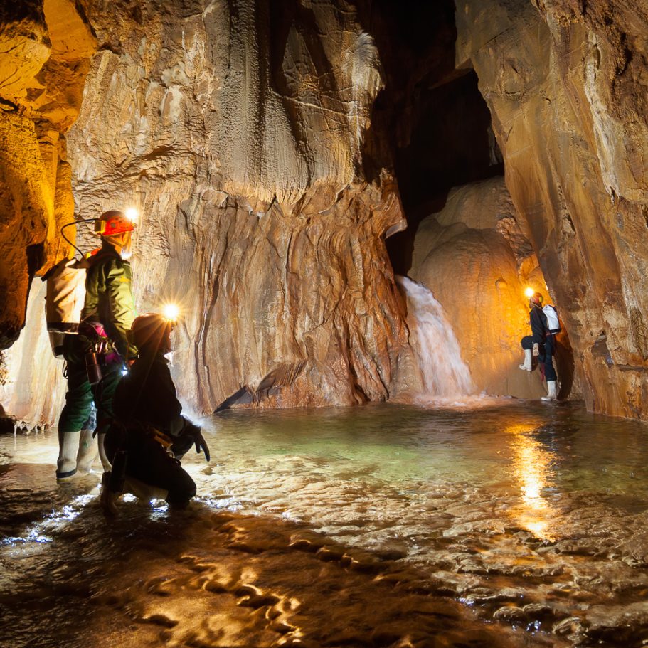 Cavers in large passage with underground river and waterfall on flowstone