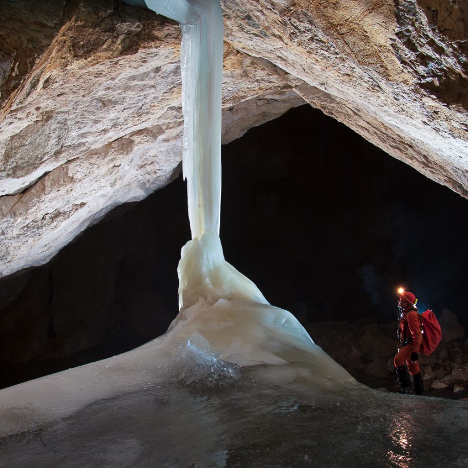 Caver passing an ice column in a large cave passage
